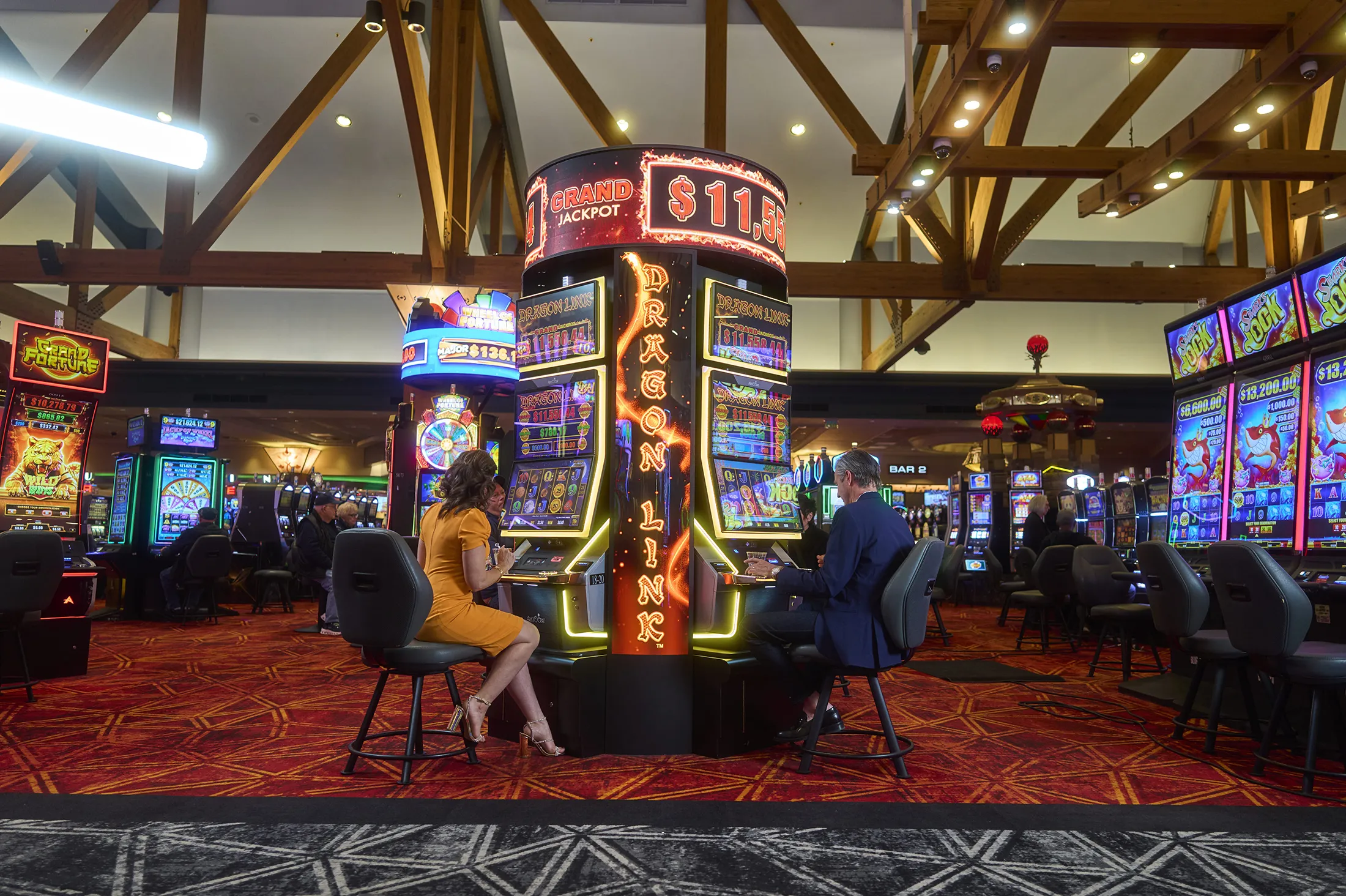 Woman and man playing slots machines seperately in large casino.