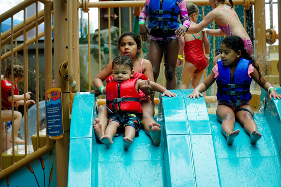 Multiple kids at a waterpark sliding fown a teal slide with a life jacket on
