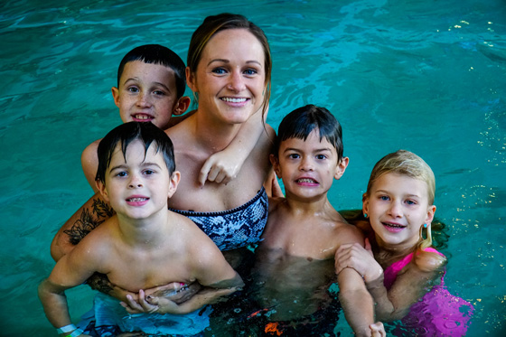 A mom with 4 kids in the water smiling.